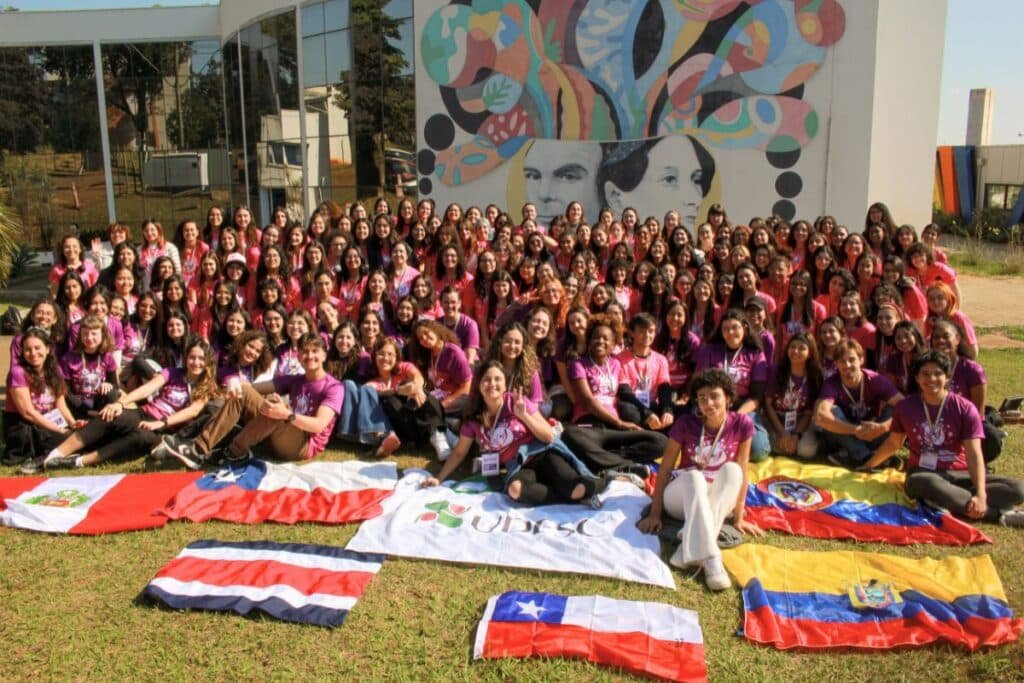 Um grupo de mulheres sentadas em um gramado. Todas estão de camisas rosas