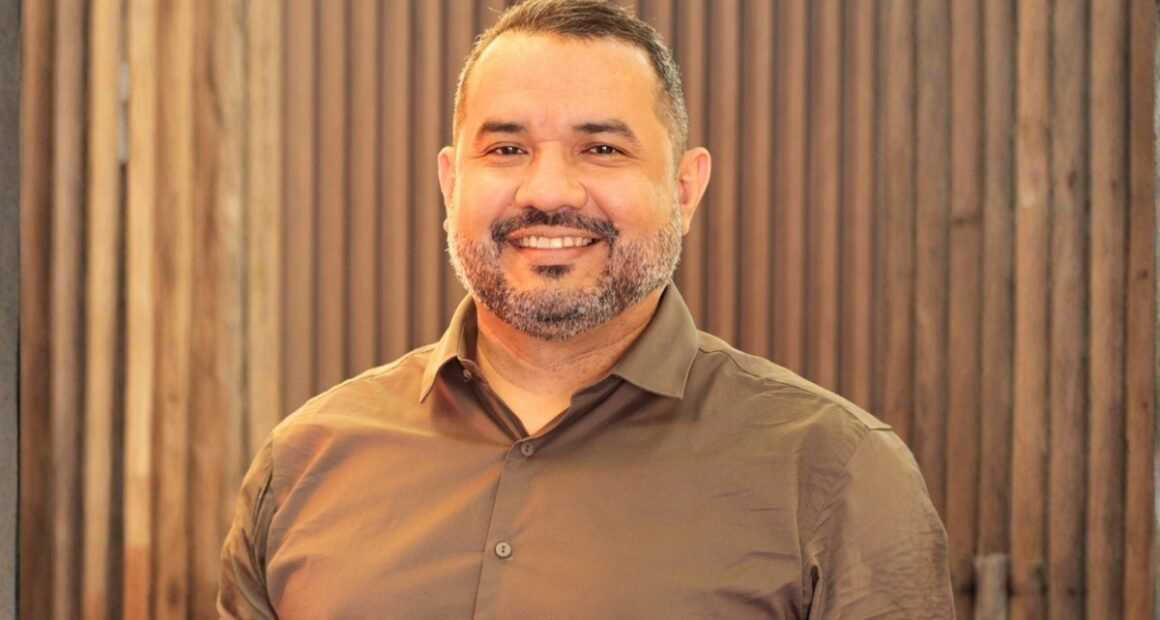 homem com barba grisalha olhando para frente e sorrindo usando camisa marrom claro