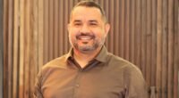 homem com barba grisalha olhando para frente e sorrindo usando camisa marrom claro