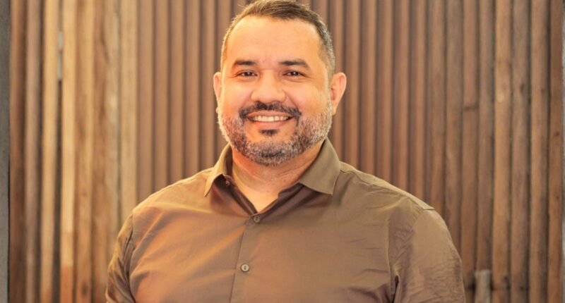 homem com barba grisalha olhando para frente e sorrindo usando camisa marrom claro
