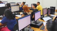 pessoas em sala de aula de informática sentadas olhando para monitores de computador