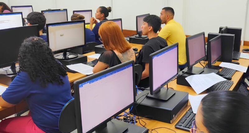 pessoas em sala de aula de informática sentadas olhando para monitores de computador