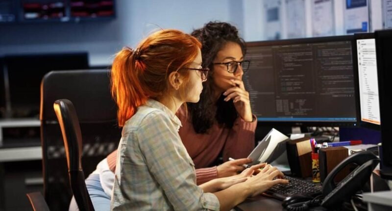 duas mulheres sentadas olhando para a tela de um computador