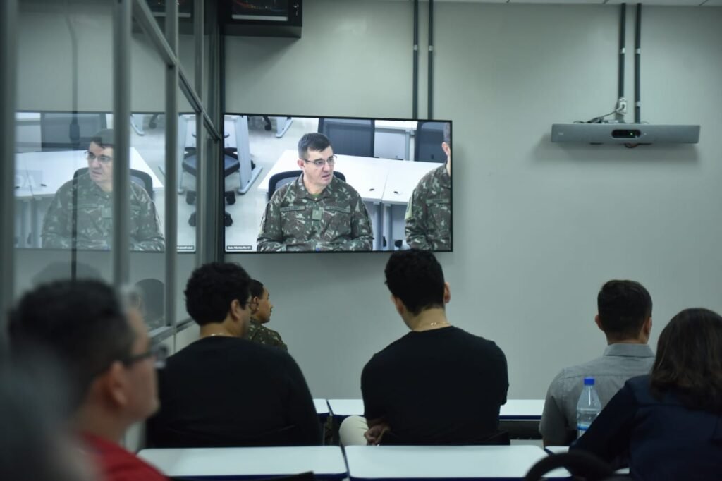 Pessoas sentadas em sala de aula olhando para um televisao
