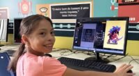menina sentada na frente do computador. ela usa camisa rosa