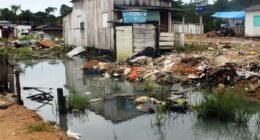 casa de madeira a beira de um igarapé com lixo nas margens
